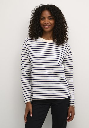 Long-sleeve shirt in ivory with navy horizontal stripes. Features a rounded neckline and relaxed fit. Paired with black pants.