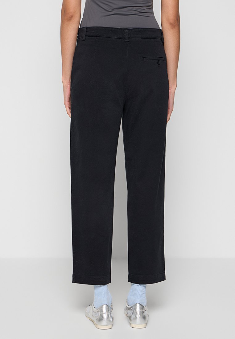 Schwarze, weit geschnittene Hosen aus Baumwolle mit glatter Textur. Verfügt über eine einzelne Gesäßtasche und eine leicht verkürzte Länge.