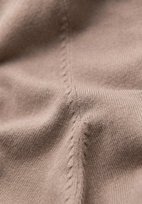 Tessuto lavorato a maglia marrone chiaro con una fine trama, caratterizzato da cuciture visibili e una superficie liscia.