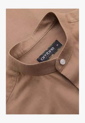 Brązowa, strukturalna koszula z podwyższonym kołnierzykiem i jednym białym guzikiem. Metka z napisem "ambre" w czarno-zielonym wzorze.