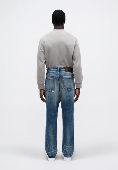 Sudadera gris y jeans azules, con un corte relajado, lavado desgastado, dos bolsillos traseros y una etiqueta de cuero marrón en la cintura.