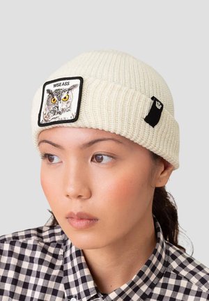 Beanie di maglia crema con texture a coste, caratterizzato da una toppa quadrata che raffigura un gufo e il testo "WISE ASS", oltre a un piccolo accento nero.