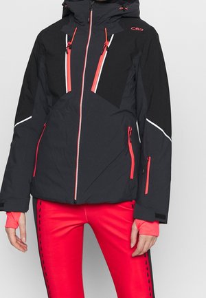 Schwarze und rote Winterjacke zum Reißverschluss mit Kapuze, mit roten Reißverschluss-Akzenten und weißen reflektierenden Details, getragen zu leuchtend roten Leggings.