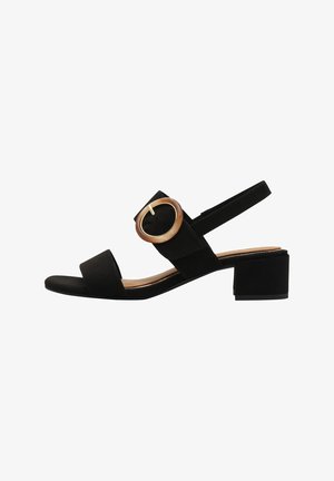 Sandale en daim noir avec de larges brides, un talon carré et un grand accent de boucle ronde en matériau clair.