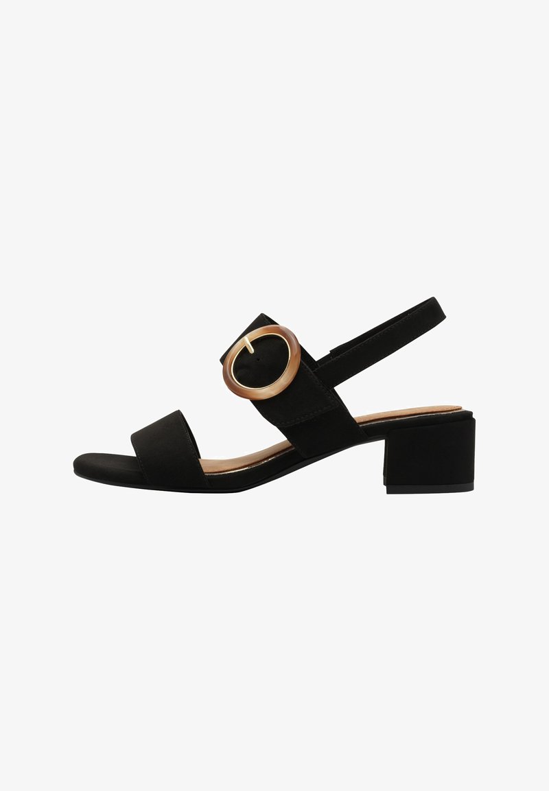 Sandale en daim noir avec de larges brides, un talon carré et un grand accent de boucle ronde en matériau clair.