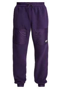 Fioletowe dresy z polaru z dwoma przednimi kieszeniami, elastycznym pasem i ściągaczami u dołu. Posiadają teksturowaną powierzchnię polaru oraz błyszczące akcenty.