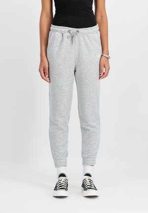 Pantalons de survêtement gris avec taille à cordon, chevilles côtelées et texture lisse. Associés à des baskets noires et des chaussettes blanches de type crew.