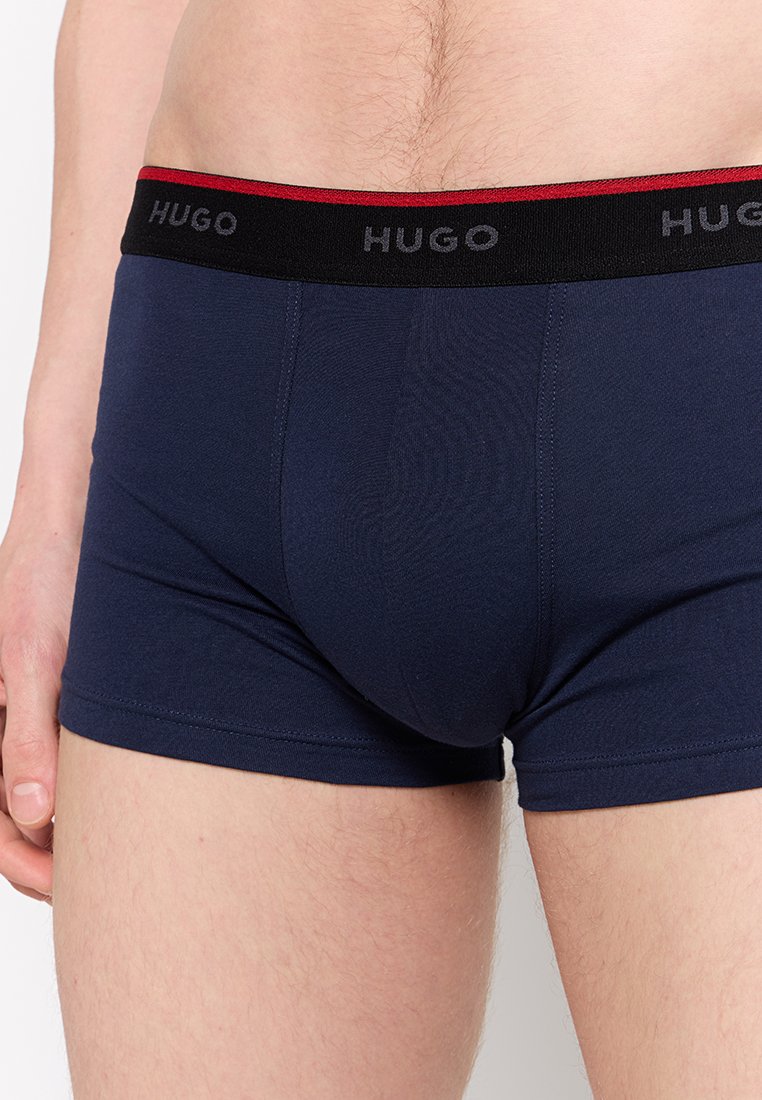 Marineblaue Baumwollboxershorts mit einem elastischen Bund in Schwarz und Rot, der das "HUGO"-Logo trägt. Sie haben eine glatte Textur und ein figurbetontes Design.
