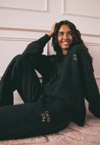 Schwarzes Strick-Lounge-Set mit Kapuzenoberteil und lockeren Hosen, mit "LUCKY STAR" in Gold gestickt. Weicher Stoff und entspannter Schnitt.