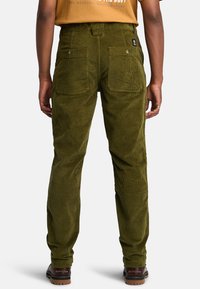 Pantaloni in corduroy verde con una finitura testurizzata, dotati di due tasche posteriori e cuciture visibili; indossati con un boot marrone.