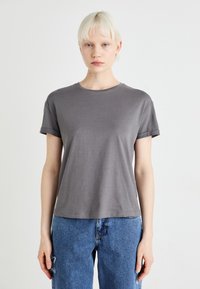 Grå t-skjorte med kort erme laget av mykt stoff med rund hals og rullet erme, sammen med blå denimbukser.
