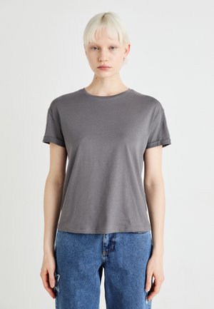 Grå t-skjorte med kort erme laget av mykt stoff med rund hals og rullet erme, sammen med blå denimbukser.