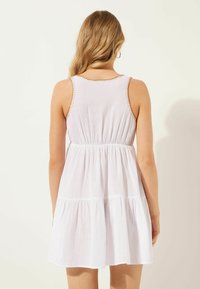 Mouwloze witte jurk met een gathered taille, een gelaagde rok en contrasterende stiksels langs de halslijn en armsgaten. Lichte stof structuur.
