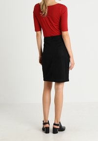 Un haut rouge ajusté à manches courtes associé à une jupe crayon noire taille haute. Des chaussures noires à talons carrés avec des brides aux chevilles.