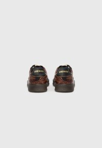 Sko med brun slangeskindsmønster og sorte hælaccentuer, samt en tekstureret sål, hvor mærkenavnet "Steve Madden" er præsenteret på hælen.