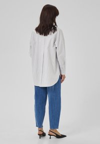 Gestreifte Langarmbluse in Weiß und Grau mit abgerundetem Saum, kombiniert mit blauen Jeans und schwarzen Slingback-Absätzen.