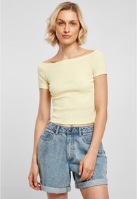 Gul ribbad off-shoulder topp med korta ärmar, parat med högmidjade, uppvikta blå denimshorts. Slät textur, avslappnad design.