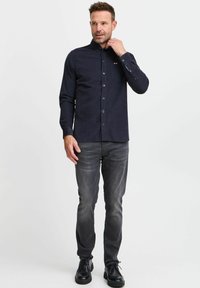 Navy button-up shirt met een kraag, een borstzak en lange mouwen. Draag het met grijze jeans en zwarte schoenen, met een gladde textuur.