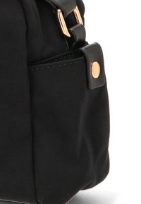 Bolso de tela negro con forma estructurada, que presenta un pequeño bolsillo exterior, herrajes en tono dorado y textura suave.