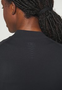 Μαύρο αθλητικό μπλουζάκι με ψηλό λαιμό, λείο υλικό και διακριτό σχέδιο κατά μήκος της πλάτης.