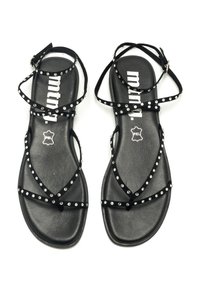 Sandalias planas negras con un diseño minimalista, que cuentan con múltiples correas entrecruzadas adornadas con tachuelas plateadas y una suela mate texturizada.