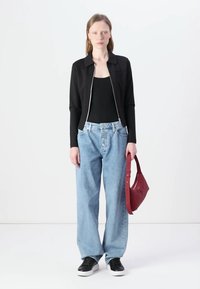 Black zip-up jacket over a black top, paired with light blue high-waisted wide-leg jeans and black sneakers, holding a red bag.