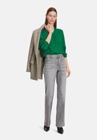 Green blouse with three-quarter sleeves, paired with high-waisted gray jeans. The outfit includes a light gray blazer and black pointed shoes.