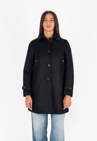 Cappotto di lana nero con colletto, chiusura frontale con bottoni e tasche laterali. Presenta maniche lunghe con dettagli a bottoni.