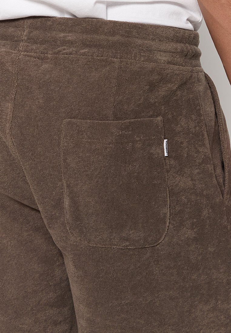 Braune Jogginghosen aus einem weichen, strukturierten Stoff mit einer rechteckigen Gesäßtasche und einem kleinen Etikett nahe dem Bund.