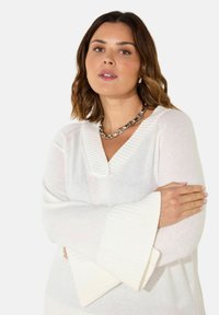 Maglione bianco a maglia con scollatura a V e maniche a coste larghe. Tessuto liscio, presenta una vestibilità morbida e dettagli orizzontali delicati.