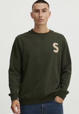 Ciemnozielony sweter z okrągłym dekoltem, prążkowanymi mankietami oraz dużym beżowym logo "S" po lewej stronie klatki piersiowej. Miękka, gładka tekstura.