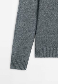Manche de pull gris tricoté avec poignets et ourlet côtelés, mettant en valeur un tissu en laine texturé sur fond blanc.