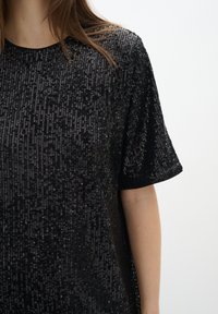 Svart kortärmad skjorta med en texturerad design som har paljetter över hela. Mjuk tyg med rund halsringning och avslappnad passform.