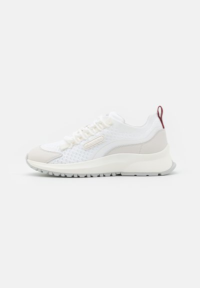 White athletic sneaker with a mesh upper, smooth leather accents, rounded toe, and a slightly elevated sole. Red pull tab at the heel.