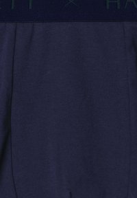 Granatowe spodnie z elastycznym, teksturowanym pasem z subtelnym napisanym logo marki w ciemnym niebieskim kolorze.