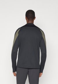 Cămașă sport cu mânecă lungă, de culoare neagră, cu accente verzi măslinii pe umeri. Fabricată dintr-un material neted și texturat, cu un design ajustat.
