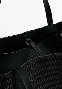 Sac fourre-tout tissé noir avec un intérieur en cuir lisse, des poignées doubles et un logo subtilement embossé sur la doublure.