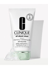 Gel nettoyant et exfoliant 2-en-1 de Clinique dans un tube blanc avec une base verte ; présente un texte noir et un emblème écologique. Des bulles à proximité.