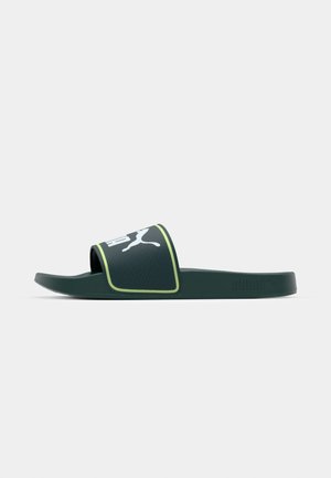 Grønne skydesandaler med en tekstureret rem, der har et hvidt Puma-logo, fremhævet af en gul kant langs kanten. Flad, ergonomisk design.