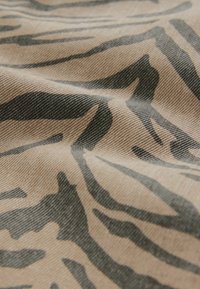 Beige tyg med mörka zebraränder, som visar en mjuk textur och en veckad yta i en närbild.