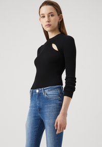 Top negro de manga larga acanalado con un detalle recortado, combinado con jeans ajustados de color azul claro que presentan bolsillos estándar y un cierre de botón.