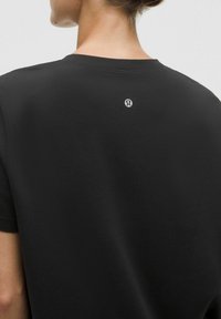 Sort atletisk t-shirt lavet af tekstureret stof, med rund hals, korte ærmer og et lille logo på den øverste ryg.