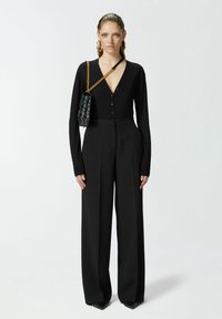 Crna pletena kardigan s gumbima, uparen s visokim crnim širokim hlačama. Dodatak: crna torba s lancem.