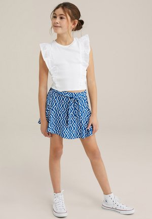 Haut en coton blanc avec des manches volantées, associé à une jupe bleue à motifs avec un lien à la taille et des baskets montantes blanches.