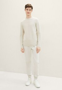 Suéter de punto de color claro con un patrón texturizado, combinado con joggers ajustados a juego y zapatillas blancas.
