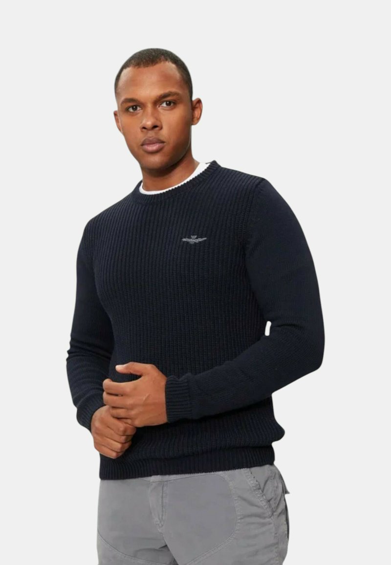 Maglione a coste in navy con scollatura a girocollo, con un colletto interno bianco a contrasto e un piccolo logo sul petto. Texture morbida.