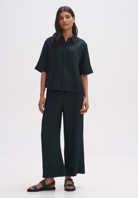 Dark green, button-down shirt with short sleeves, paired with wide-leg pants in matching textured fabric. Black sandals complete the look.