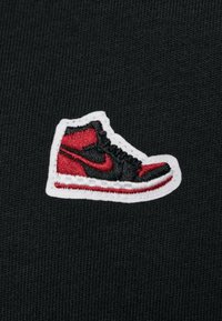 Tessuto nero con un logo di sneaker ricamato in rosso e nero contornato di bianco, caratterizzato da un design alto e da cuciture dettagliate.