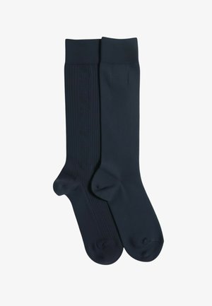 Granatowe skarpetki o różnych fakturach; jedna dziergana w prążki z subtelnym wzorem, druga gładka. Obie mają wzmocniony nosek i elastyczne mankiety.