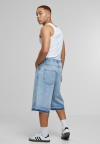 Shorts de mezclilla azul claro con un corte holgado, dobladillo deshilachado y dos bolsillos traseros. Llevados con una camiseta sin mangas blanca y zapatillas en blanco y negro.